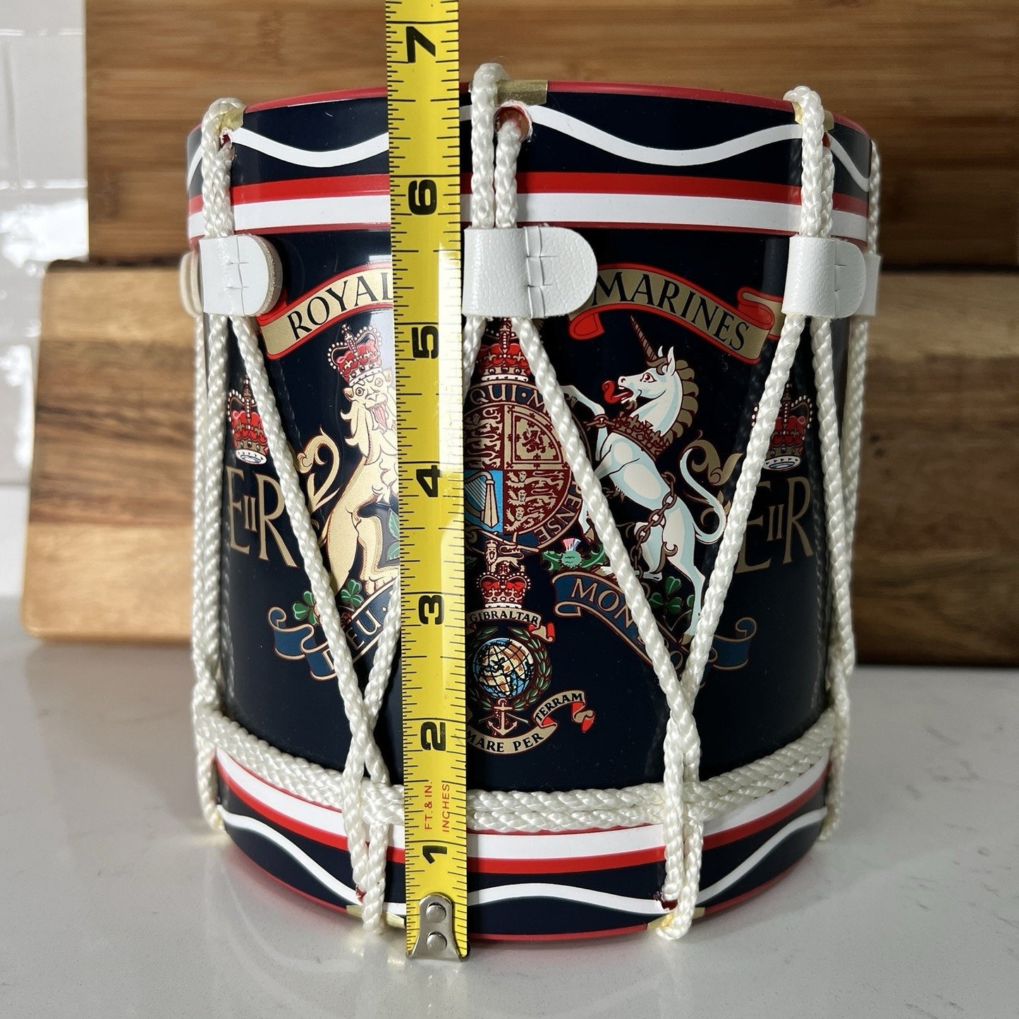 Decorative container with rope handles and a measuring tape for scale on a wooden surface.