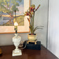 Decorative lamp and potted plant on a wooden surface with a painting in the background.
