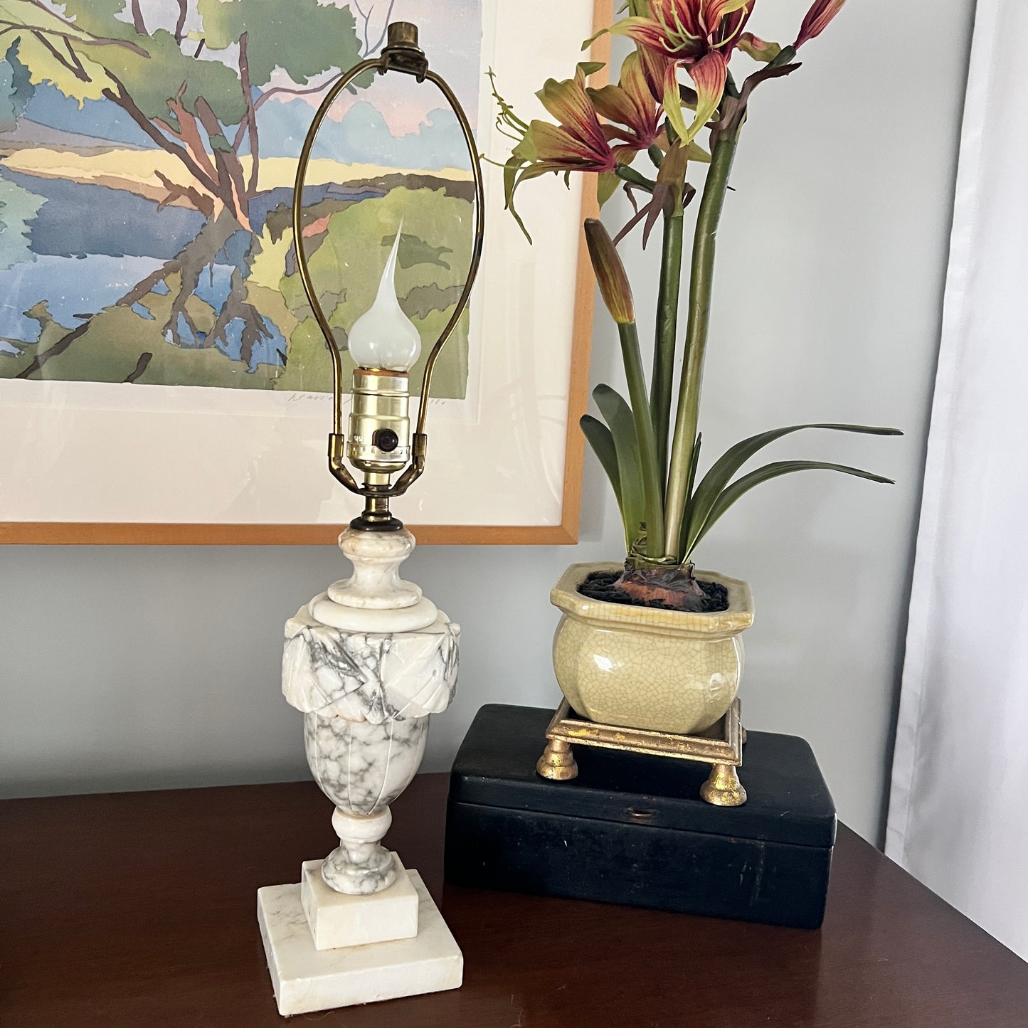 Marble lamp and potted plant on a table with a painting in the background