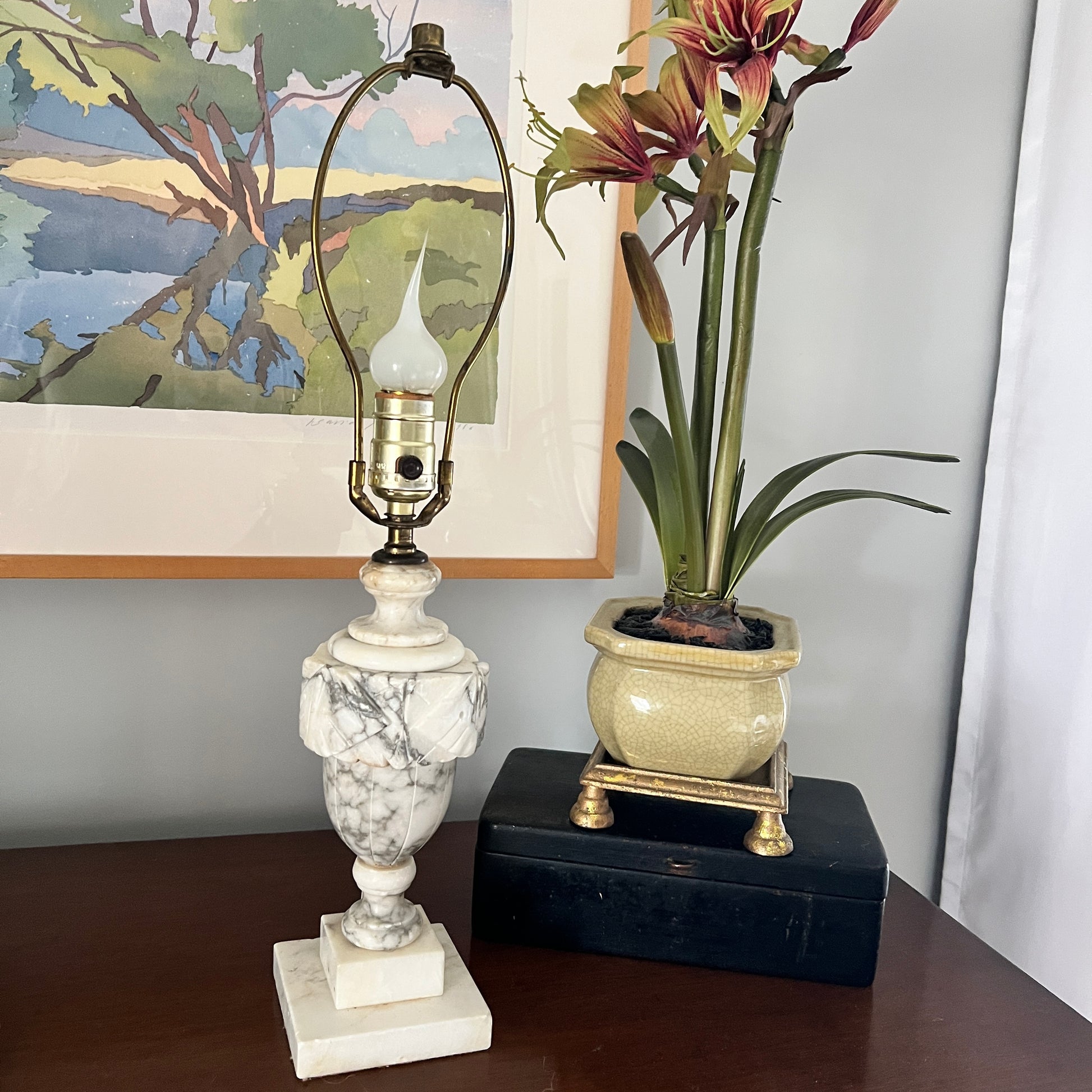 Marble lamp and potted plant on a table with a painting in the background