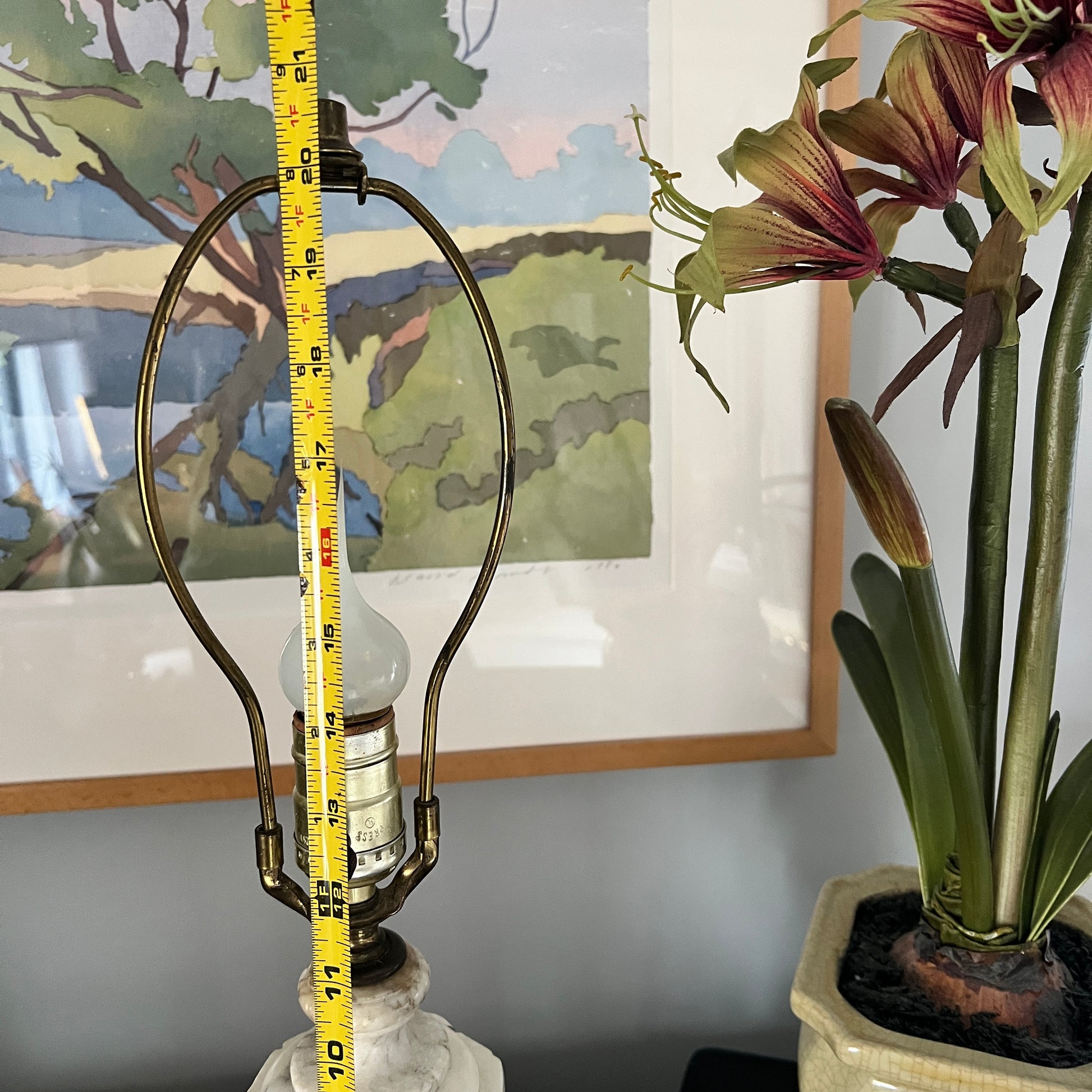 Lamp with a measuring tape against a wall with a painting and a plant.
