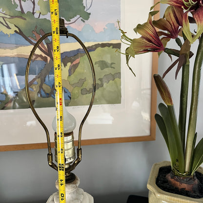 Lamp with a measuring tape against a wall with a painting and a plant.