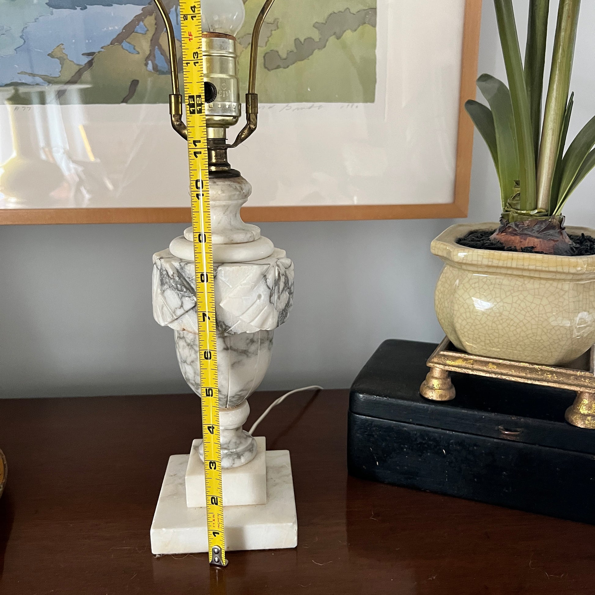 Marble lamp with a measuring tape on a table, with a plant and framed picture in the background.