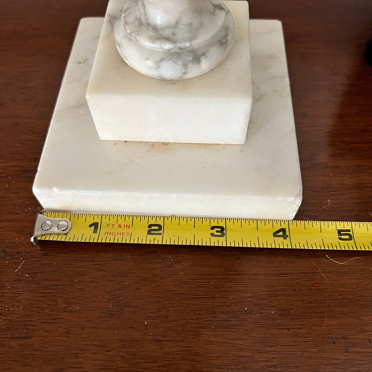 Marble pedestal with a measuring tape for scale on a wooden surface
