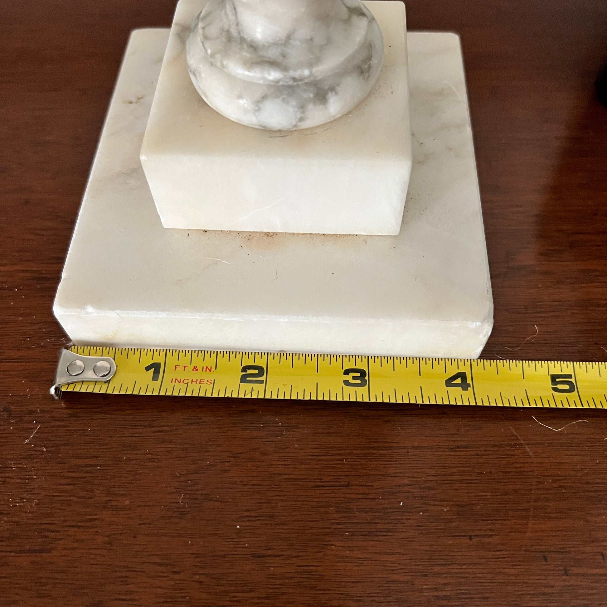 Marble pedestal with a measuring tape for scale on a wooden surface