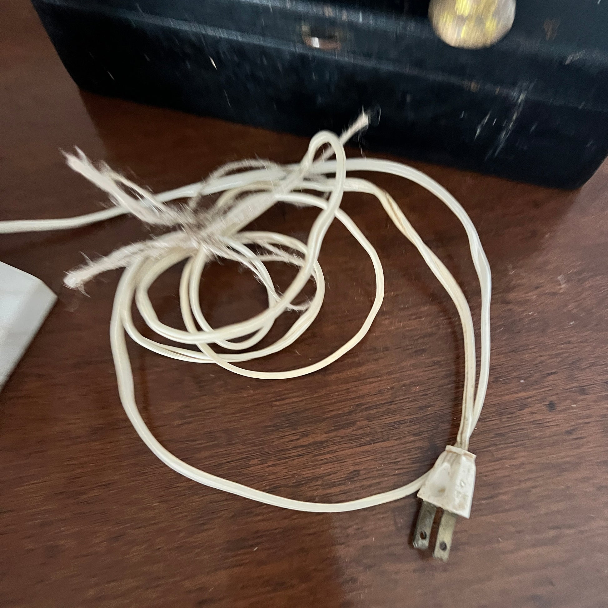 Old electrical cord on a wooden surface with a black box in the background.