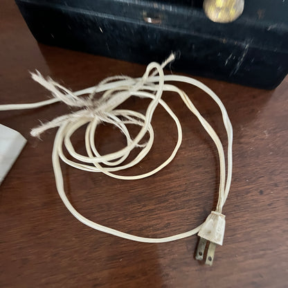Old electrical cord on a wooden surface with a black box in the background.