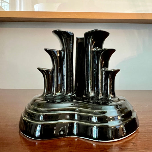Glossy black ceramic multi-stem candle holder with an Art Deco sculptural design, displayed on a wooden surface with a light background.