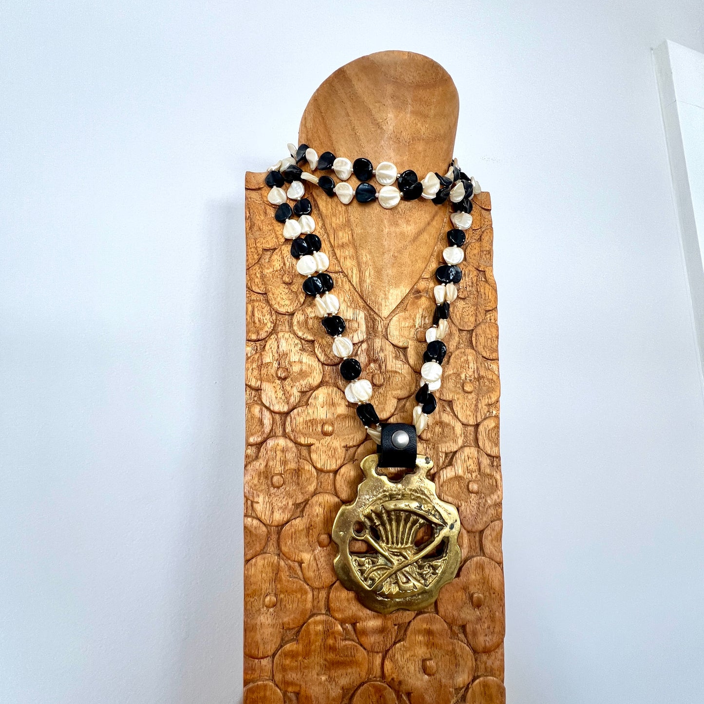 Necklace with black and white beads and a gold pendant on a wooden stand against a white background
