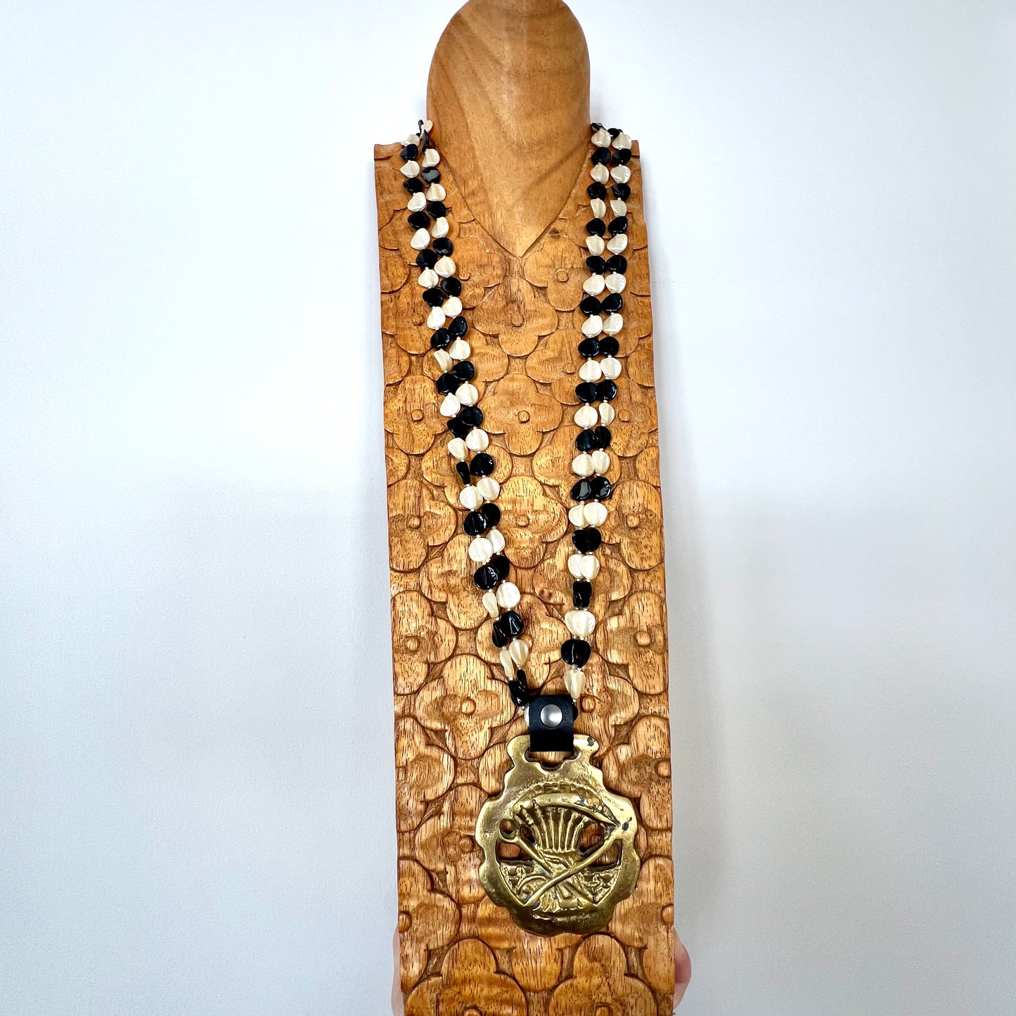 Necklace with black and white beads and a gold pendant on a wooden stand against a white background