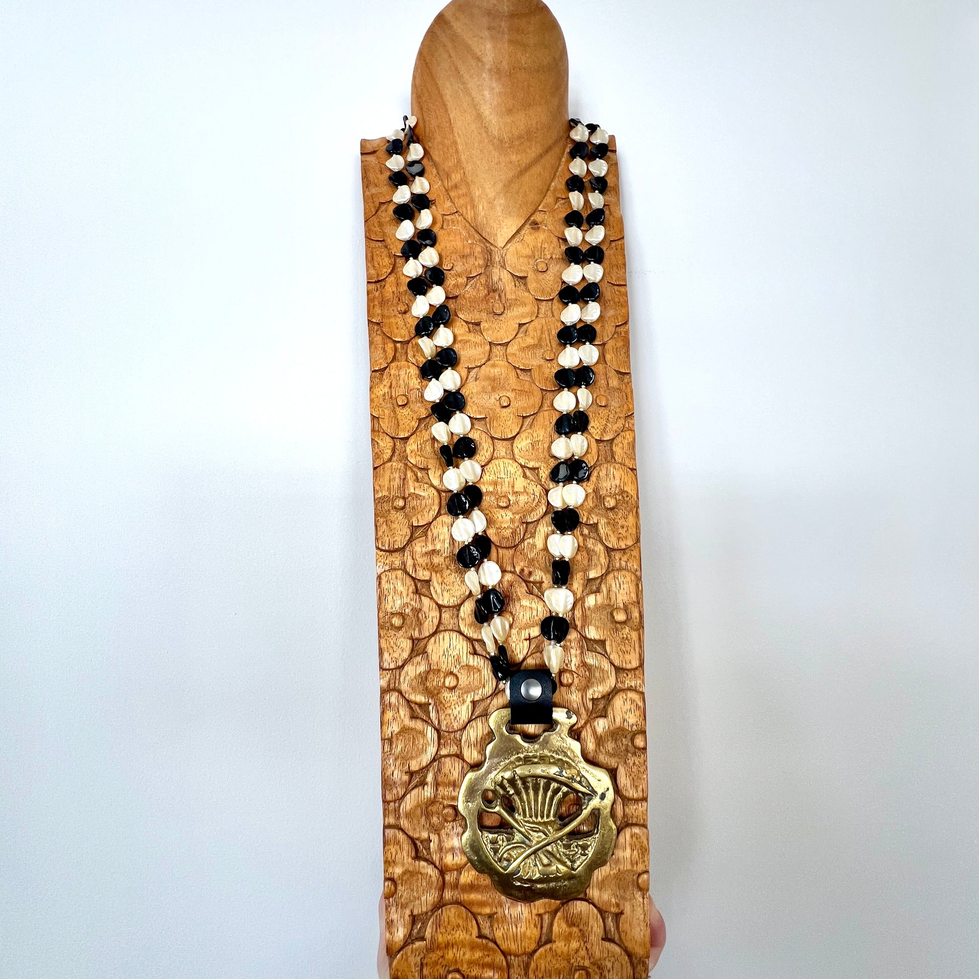 Necklace with black and white beads and a gold pendant on a wooden stand against a white background