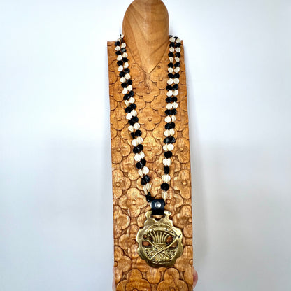 Necklace with black and white beads and a gold pendant on a wooden stand against a white background