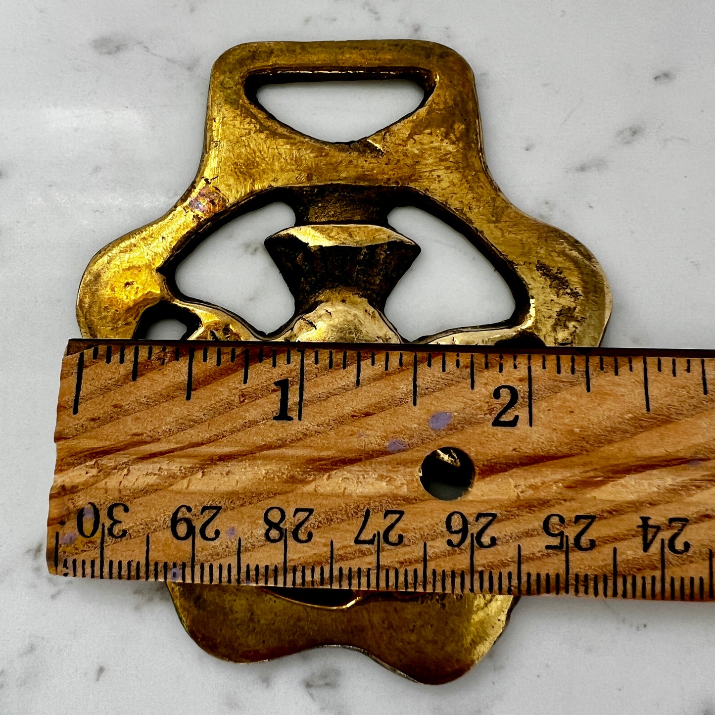 Brass medallion on a marble surface with a wooden ruler for scale.