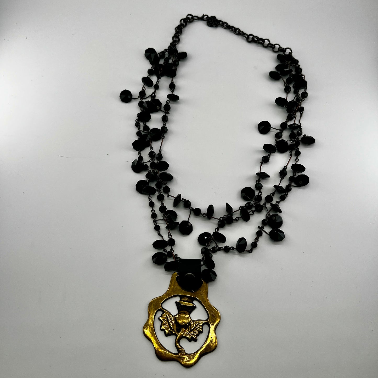 Black beaded necklace with a brass pendant on a white background