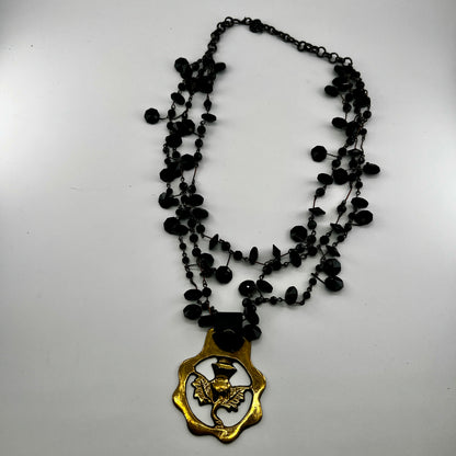Black beaded necklace with a brass pendant on a white background