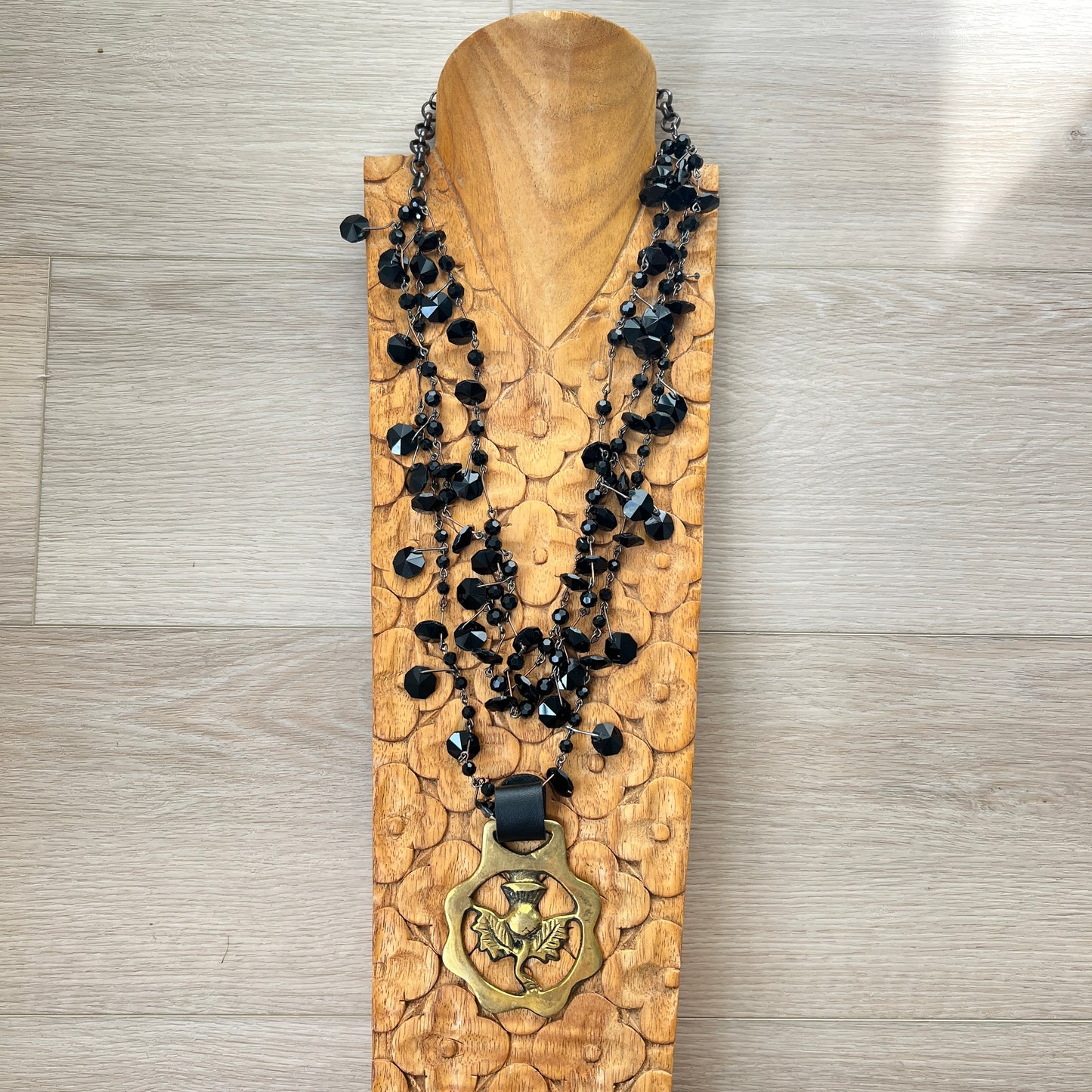 Black beaded necklace with brass medallion on wood with tan background