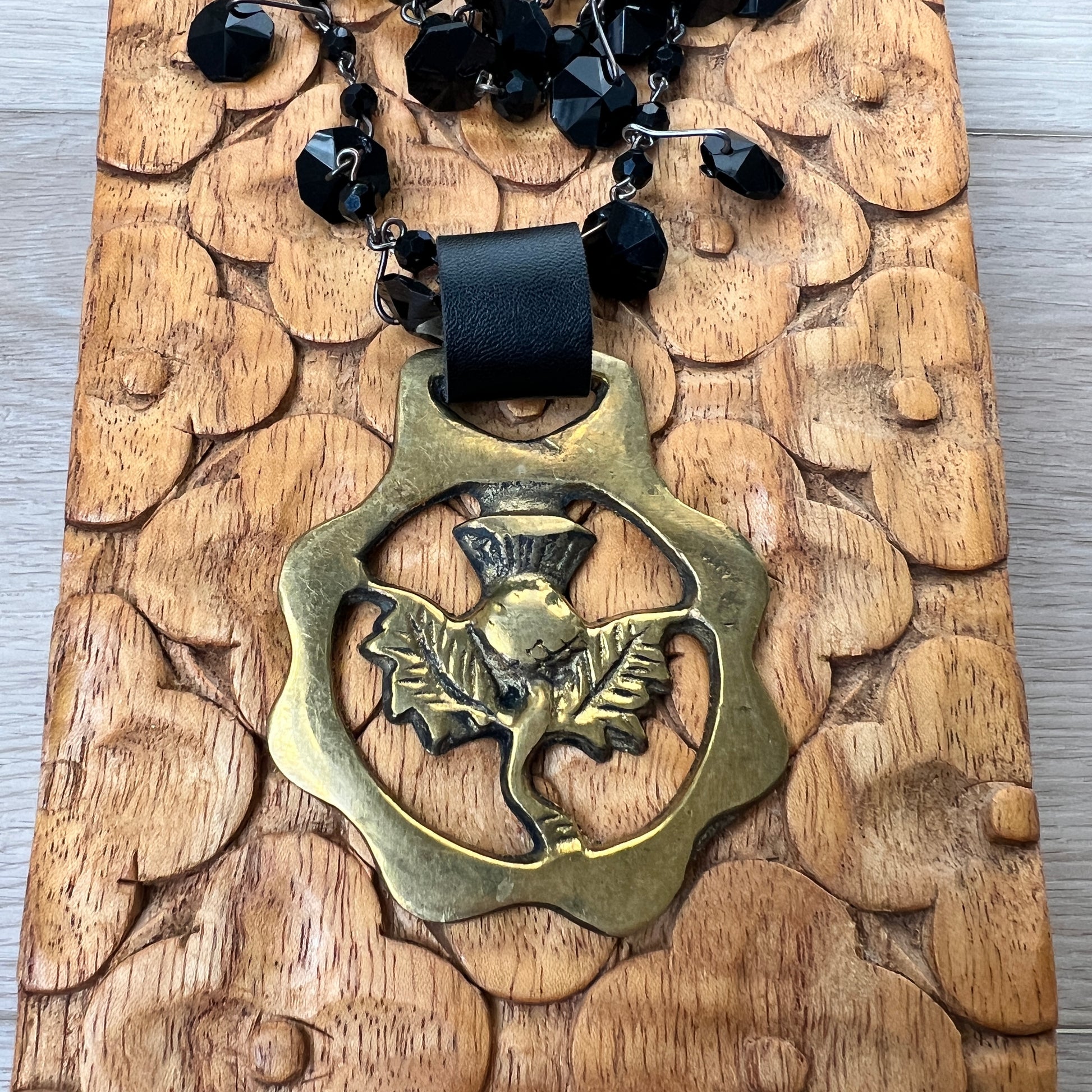 Black beaded necklace with brass medallion with leather attachment on wood with tan background