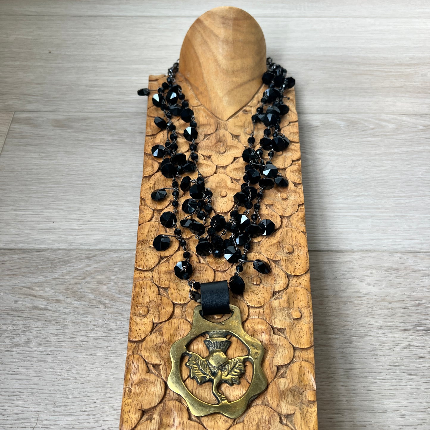 Black beaded necklace with brass medallion on wood with tan background