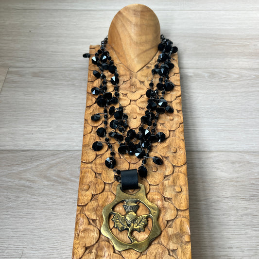 Black beaded necklace with brass medallion on wood with tan background