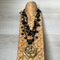Black beaded necklace with brass medallion on wood with tan background
