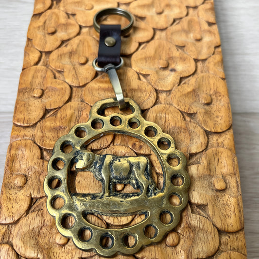 Brass keychain with cow design on a wooden surface