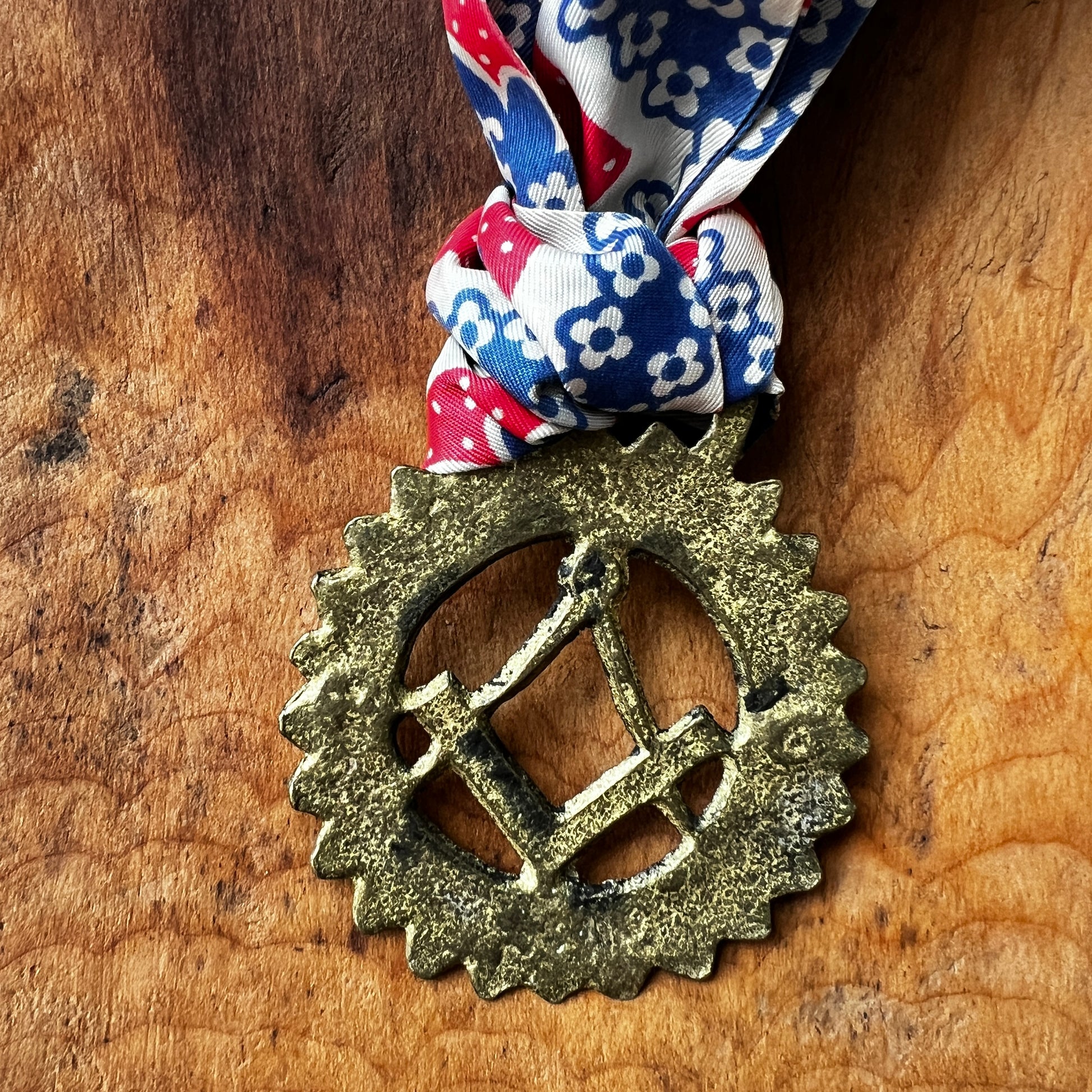 Back of Vintage Masonic square and compass brass medallion necklace with red white blue scarf. on wood surface