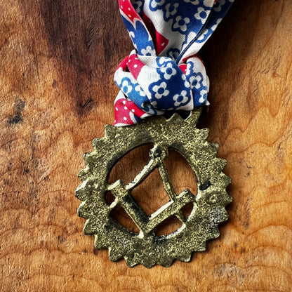 Back of Vintage Masonic square and compass brass medallion necklace with red white blue scarf. on wood surface