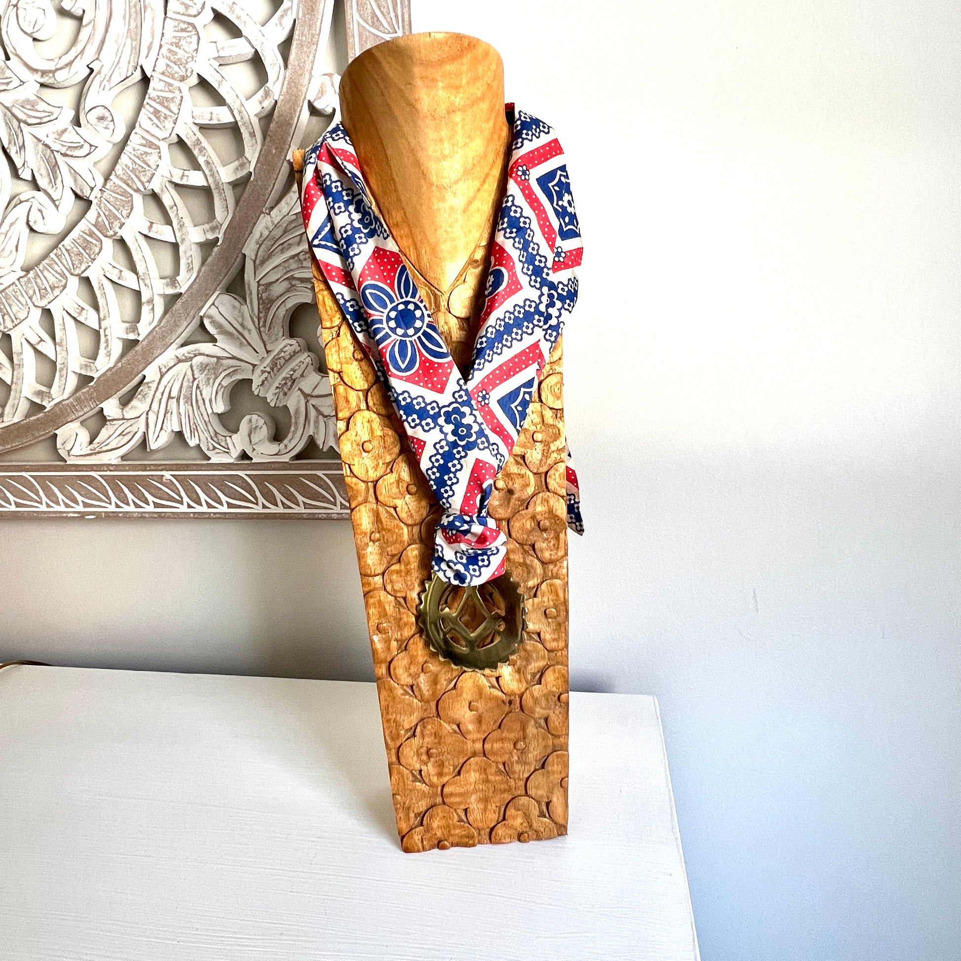 Wooden mannequin head with a patterned scarf against a decorative wall.