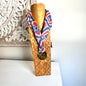 Wooden mannequin head with a patterned scarf against a decorative wall.
