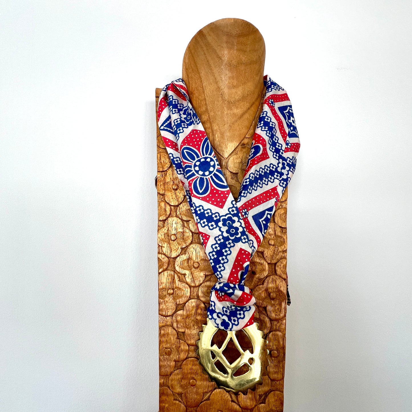 Decorative scarf with geometric pattern and gold pendant on a wooden stand against a white background