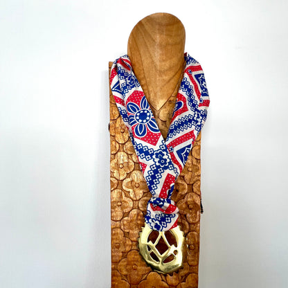 Decorative scarf with geometric pattern and gold pendant on a wooden stand against a white background