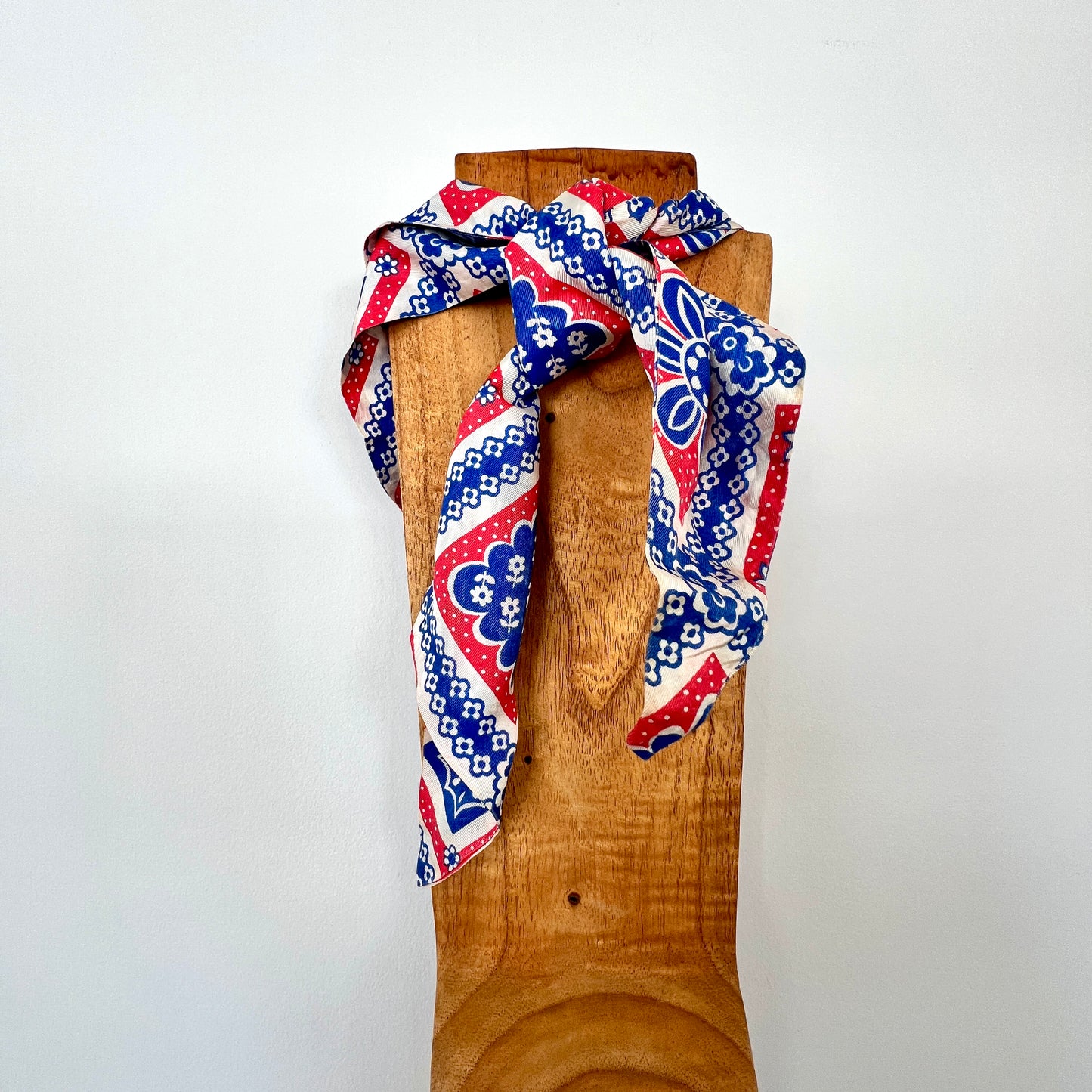 Colorful patterned scarf draped over a wooden block against a white background