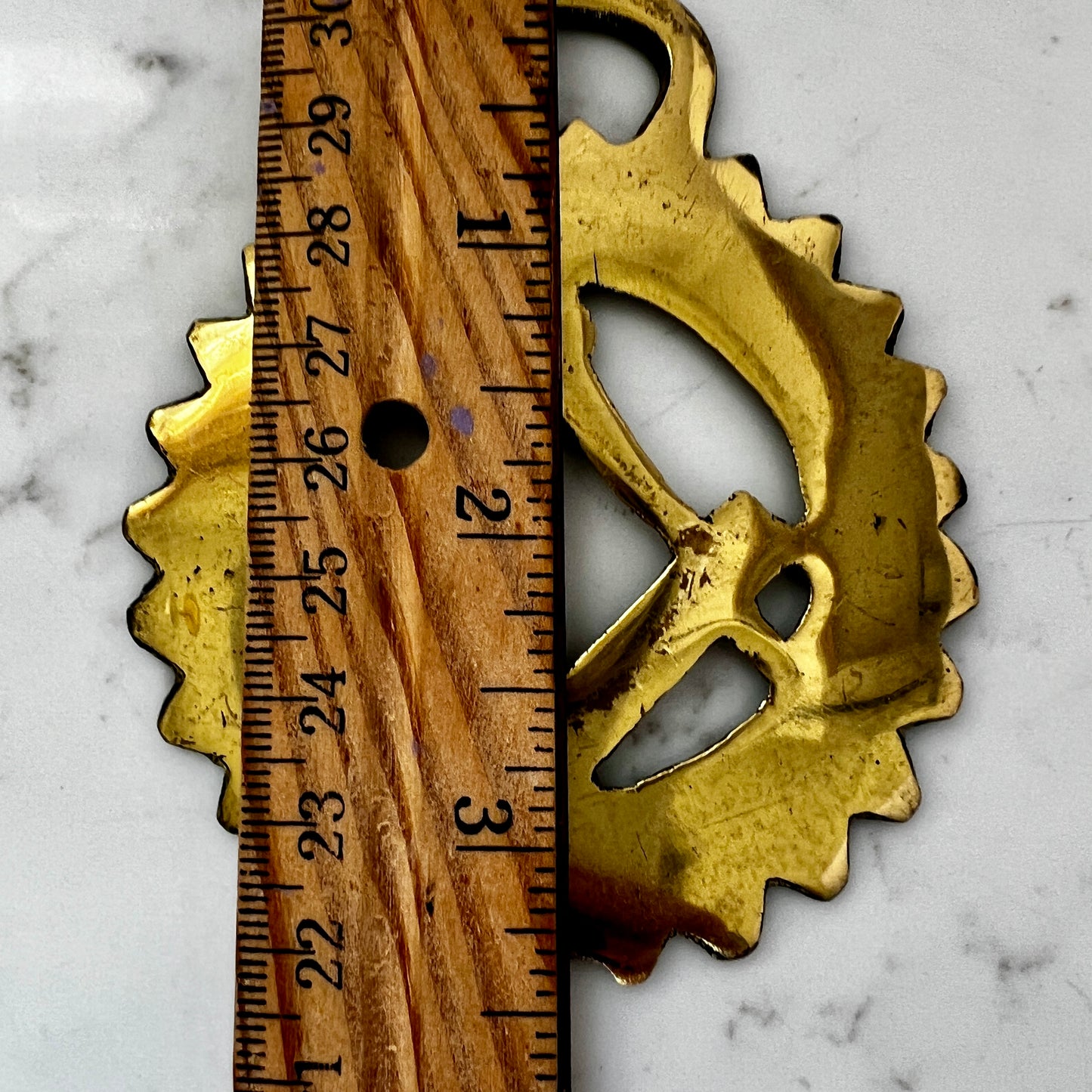 Gold metal medallion with a wooden ruler for scale on a marble surface