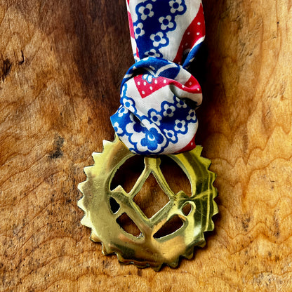 Brass gear-shaped pendant with decorative ribbon on a wooden surface