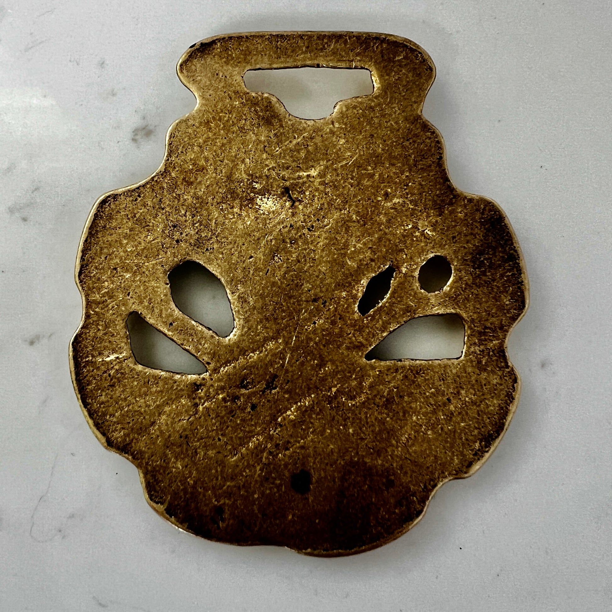 Bronze decorative object with cut-out shapes on a gray background