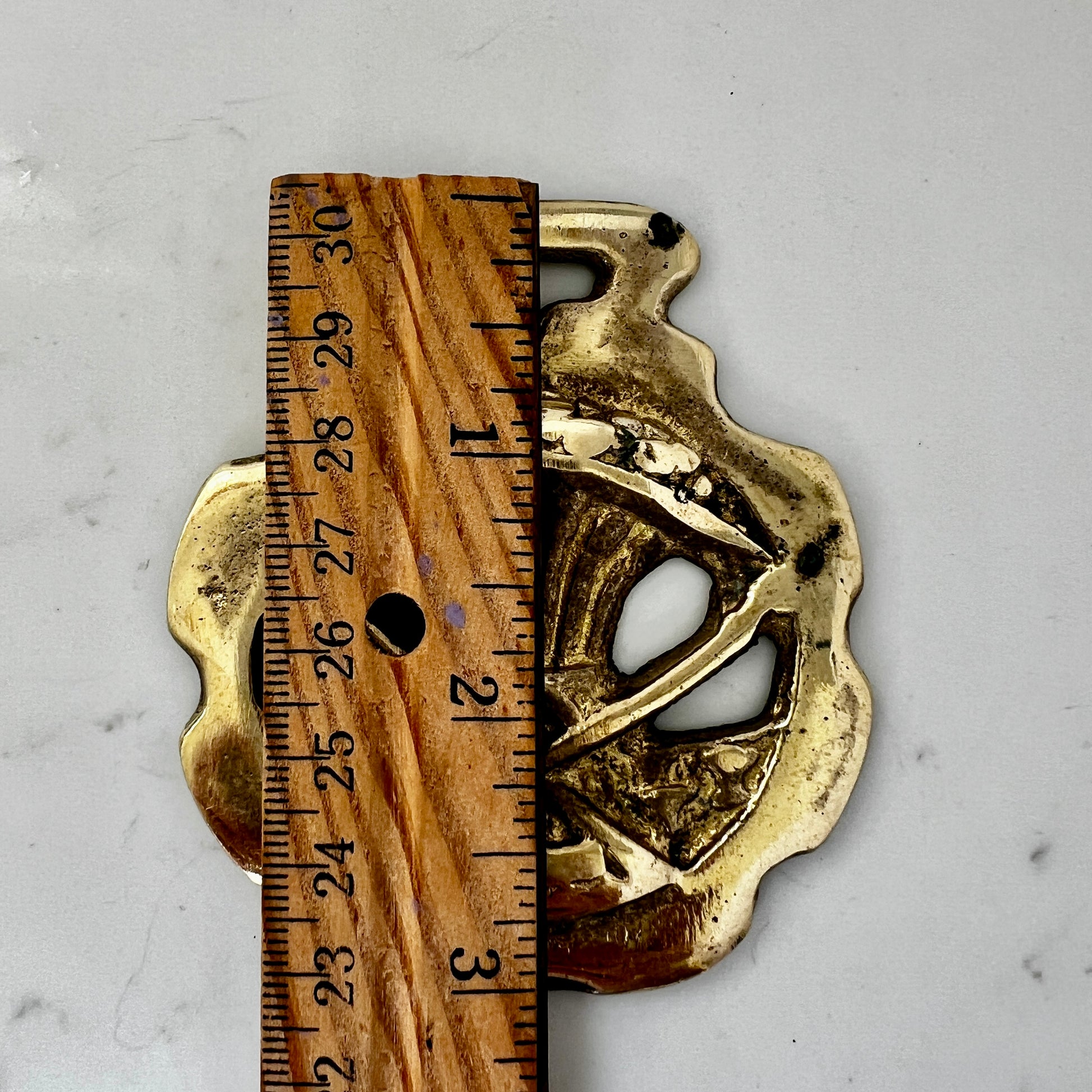 Brass decorative object next to a wooden ruler on a gray background