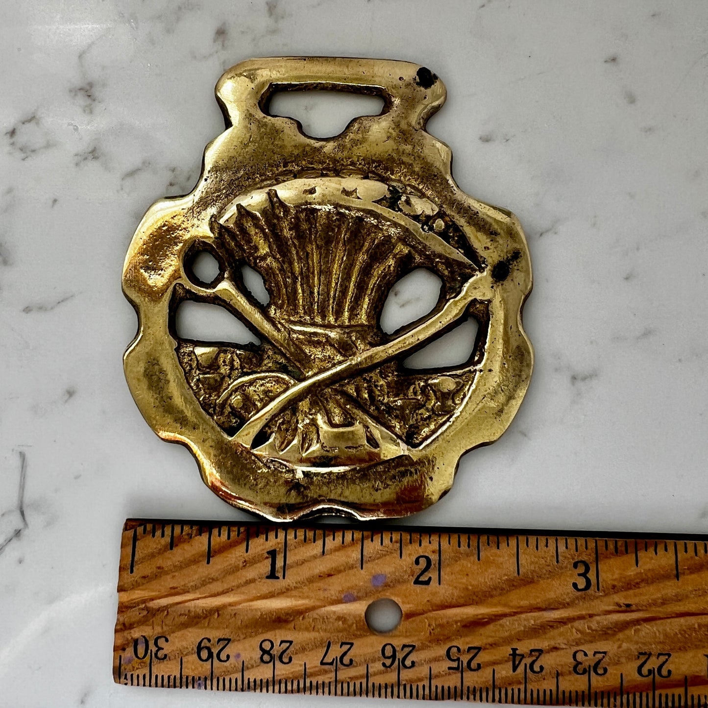 Gold decorative object with intricate design on a marble surface with a wooden ruler for scale.
