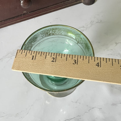 A green glass with a gold rim and floral pattern, shown with a wooden ruler to indicate its size on a white marble surface.