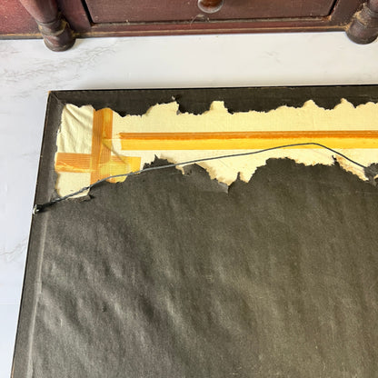 A close-up of the back of a dark gray or black rectangular mat, showing a torn edge with beige backing material and a yellow-orange adhesive strip applied to a white marble surface.