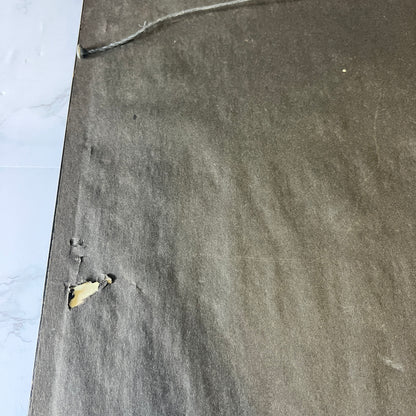 A close-up of a dark gray textured carpet or rug with a small torn section showing a beige backing, placed next to a white marble-patterned surface.