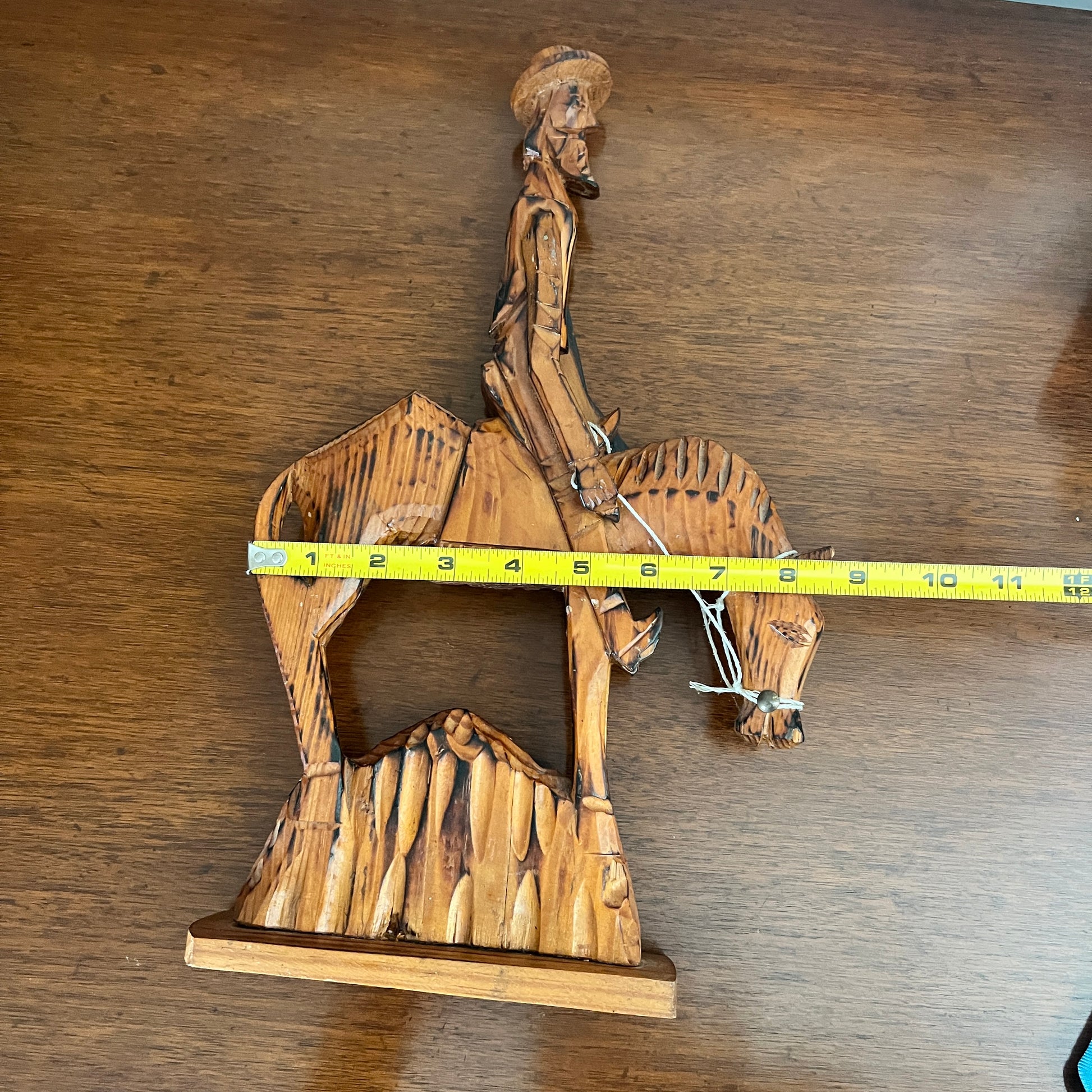 Wooden sculpture of a person on horseback with a measuring tape for scale on a wooden surface