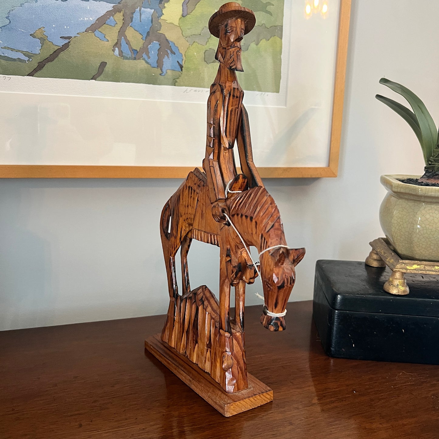 Wooden sculpture of a man on a horse with a painting in the background