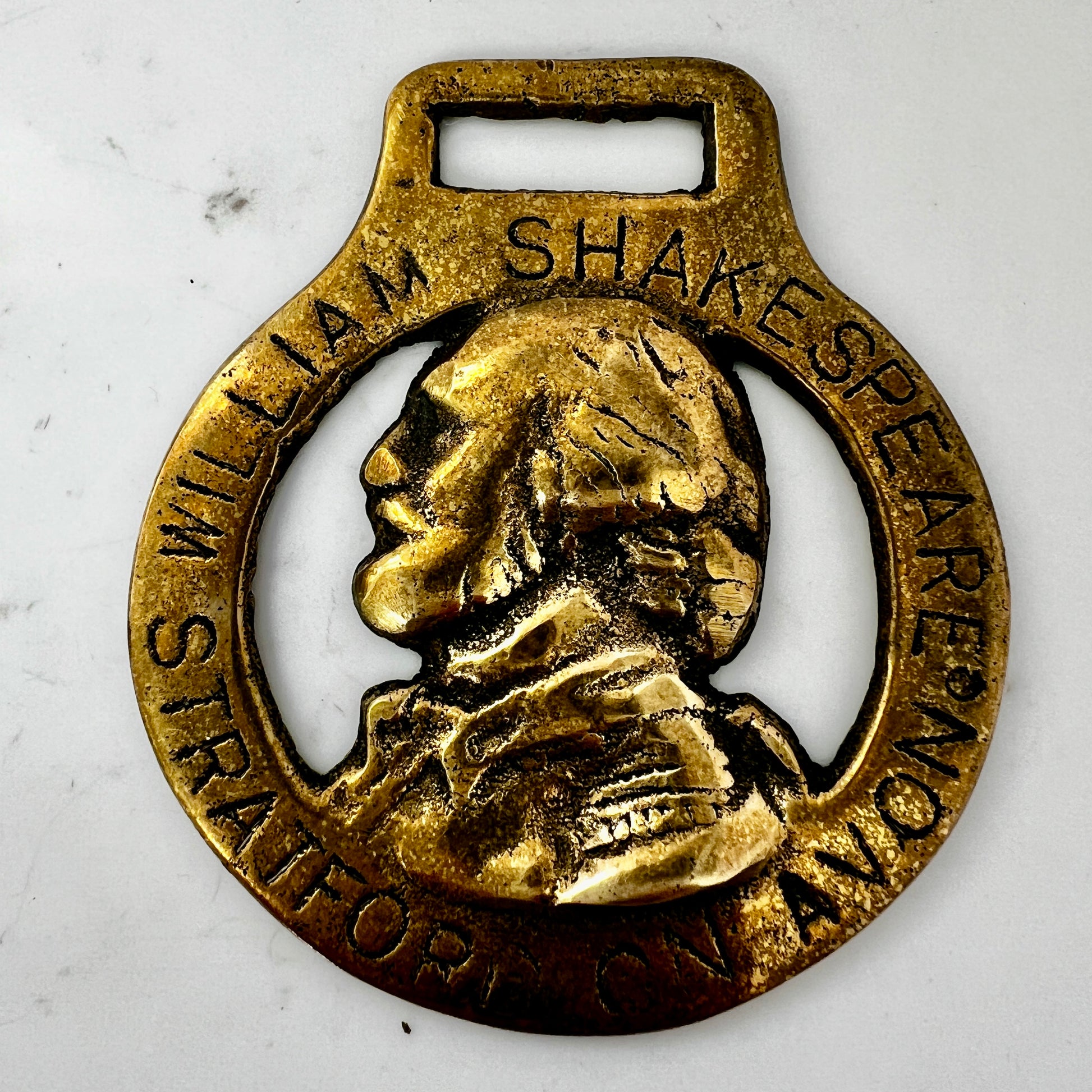 Vintage William Shakespeare horse brass medallion attached to brown leather keychain with brass ring and clip.