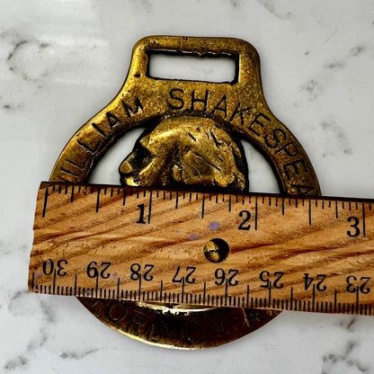 Vintage William Shakespeare horse brass medallion attached to brown leather keychain with brass ring and clip.