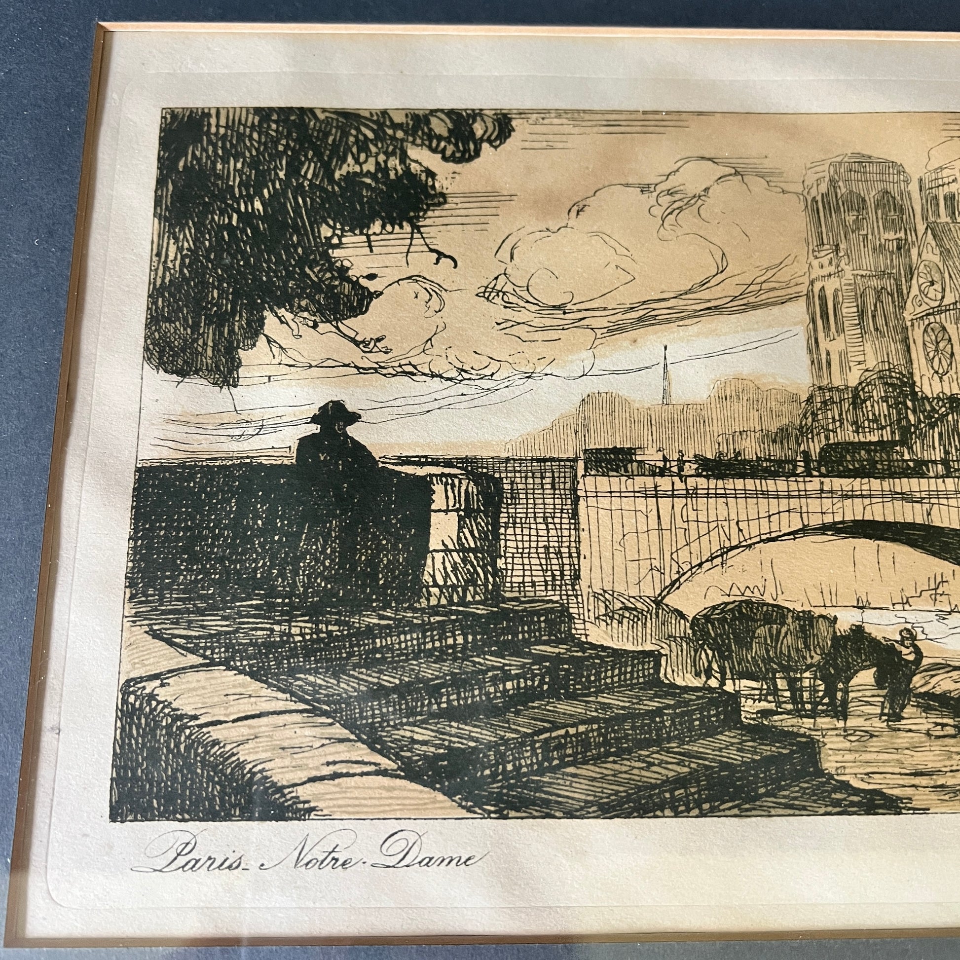 A vintage black ink sketch print of Paris Notre Dame, featuring a seated figure, a bridge, and cows in the foreground, mounted on a cream paper background.