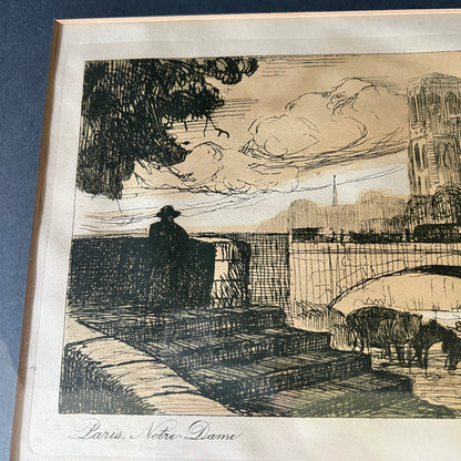 A framed black ink sketch print on aged beige paper, depicting a city scene with a bridge, a silhouetted figure, trees, and a tower. The print is mounted with a wide white mat and a light wood frame, photographed against a dark blue background.
