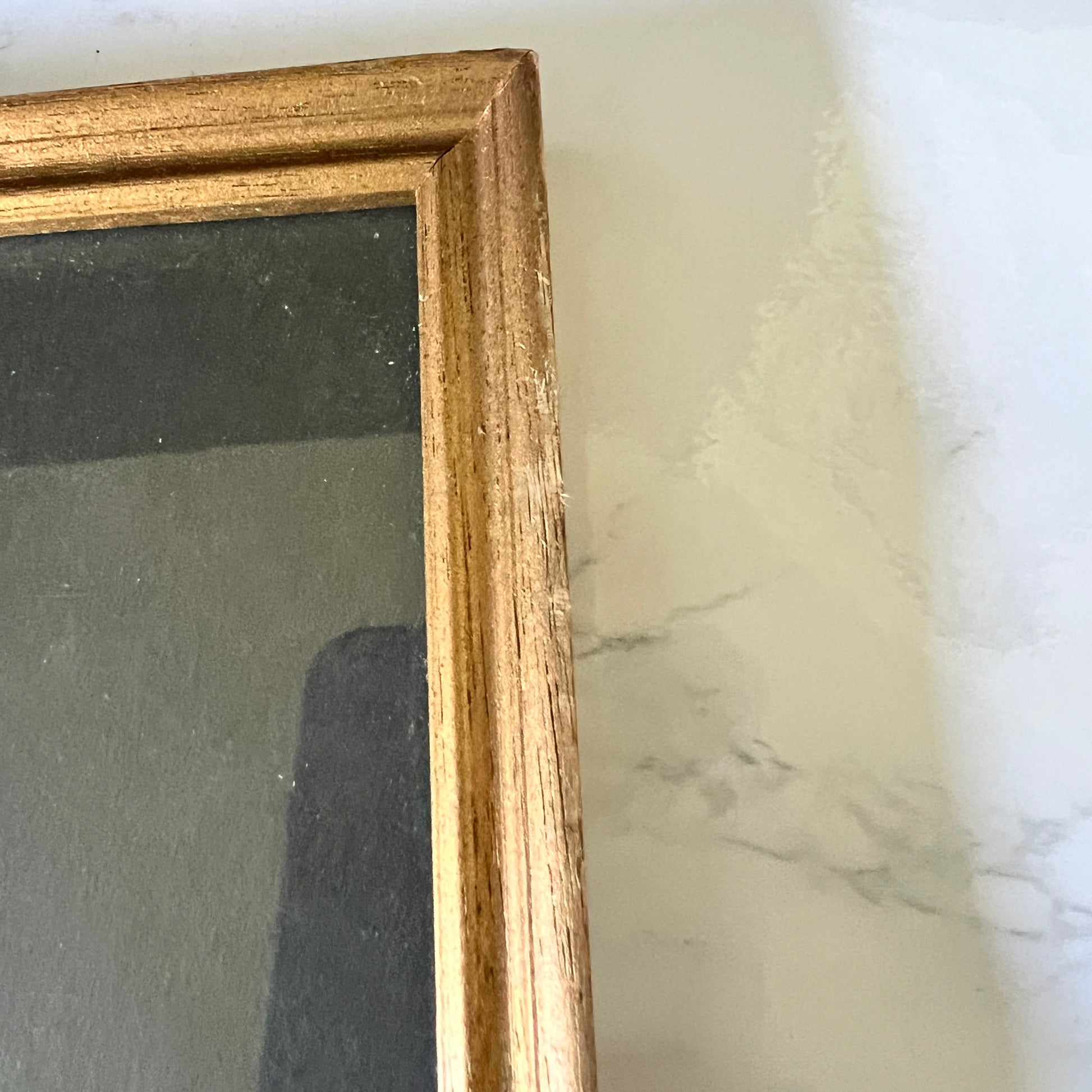 Close-up of a scuffs on gold picture frame with a dark backing, resting on a white marble-patterned surface.