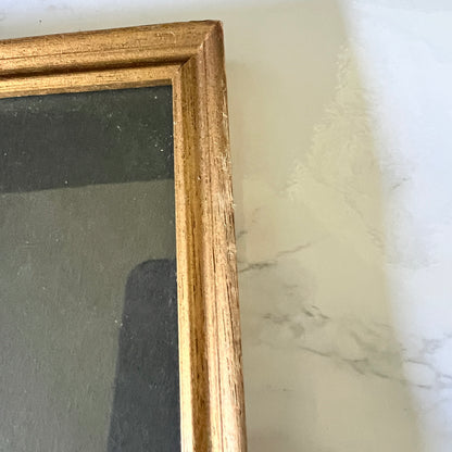 Close-up of a scuffs on gold picture frame with a dark backing, resting on a white marble-patterned surface.