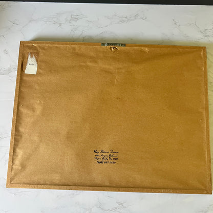 The back of a framed art print or canvas, showing a brown paper backing with handwritten identification text and a small white label, laid flat on a white marble surface.