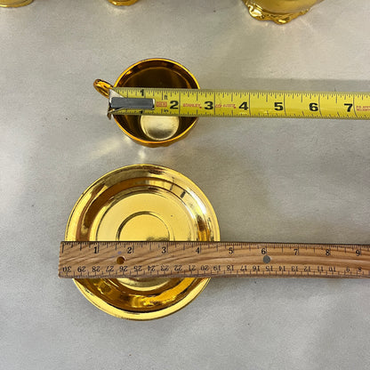 Gold-colored ceramic cup and saucer set shown with measuring tapes to indicate dimensions, on a light gray surface.